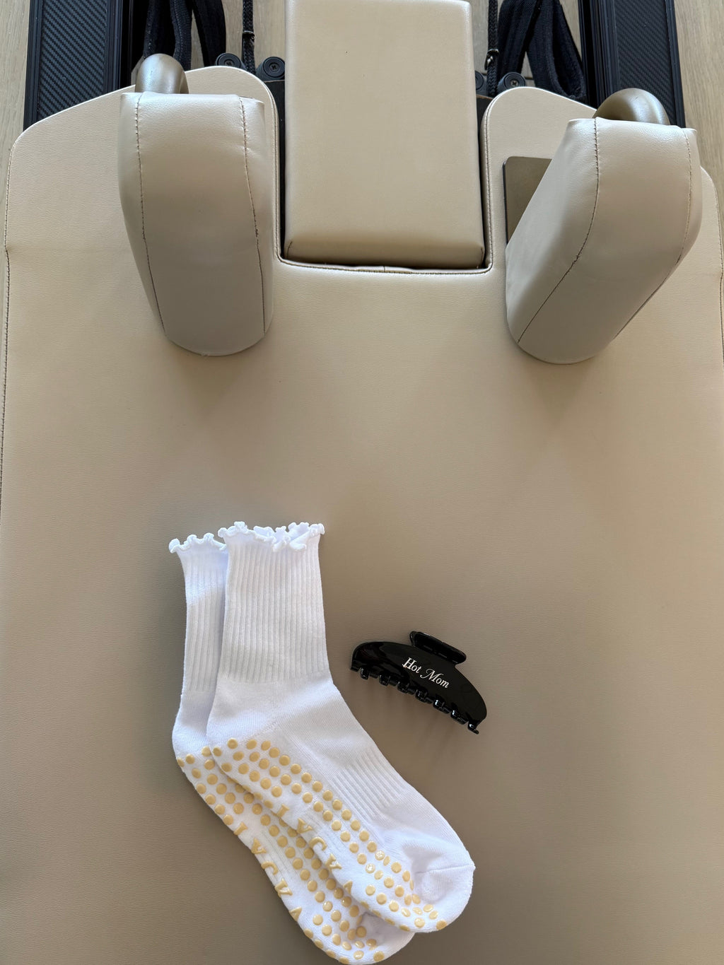 White sock with yellow grip soles next to a black hair clip that says “hot mom” on a beige surface