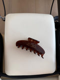 Brown hair clip with gold text “Save a horse, Ride a reformer” on a white reformer 