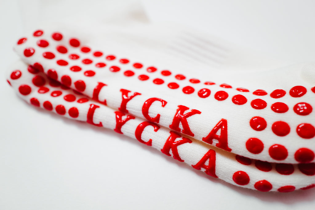 Bottom of white dolls with red polka dot gripsand 'LYCKA' text on a white background