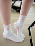 White socks with pink heart accents worn by a person on a blurred indoor background