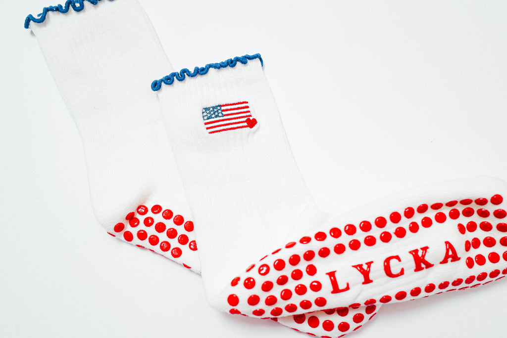 White socks with american flag embroidery with red polka dot grips saying 'LYCKA' branding on a white background