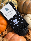Black grip socks with white polka dots and a cute ghost graphic, shown with a white hang tag reading 'LYCKA GRIP SOCKS' and styled among pumpkins and autumn leaves.