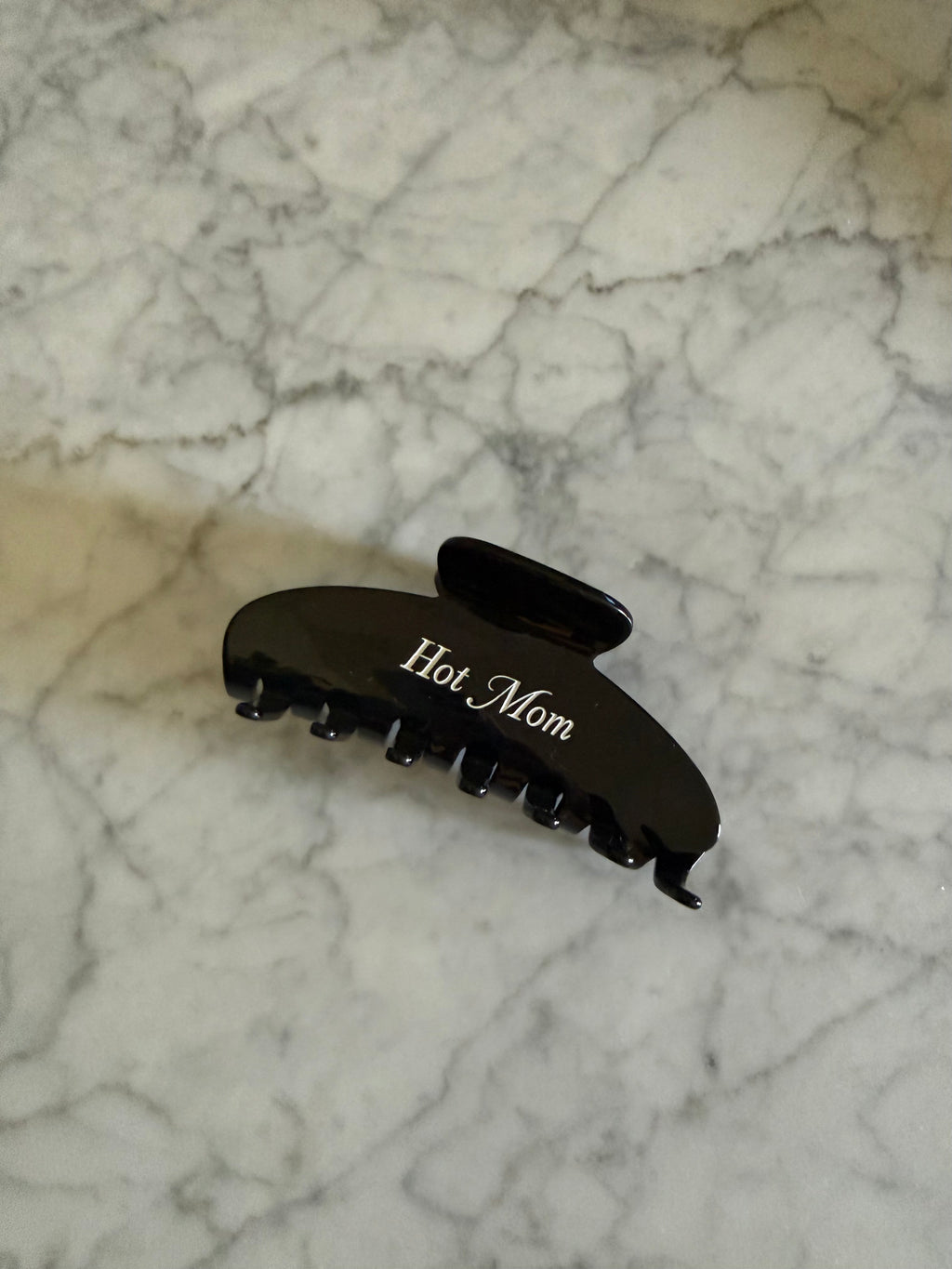 Black hair clip with 'Hot Mom' text on a marble surface
