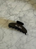 Black hair clip with 'Hot Mom' text on a marble surface