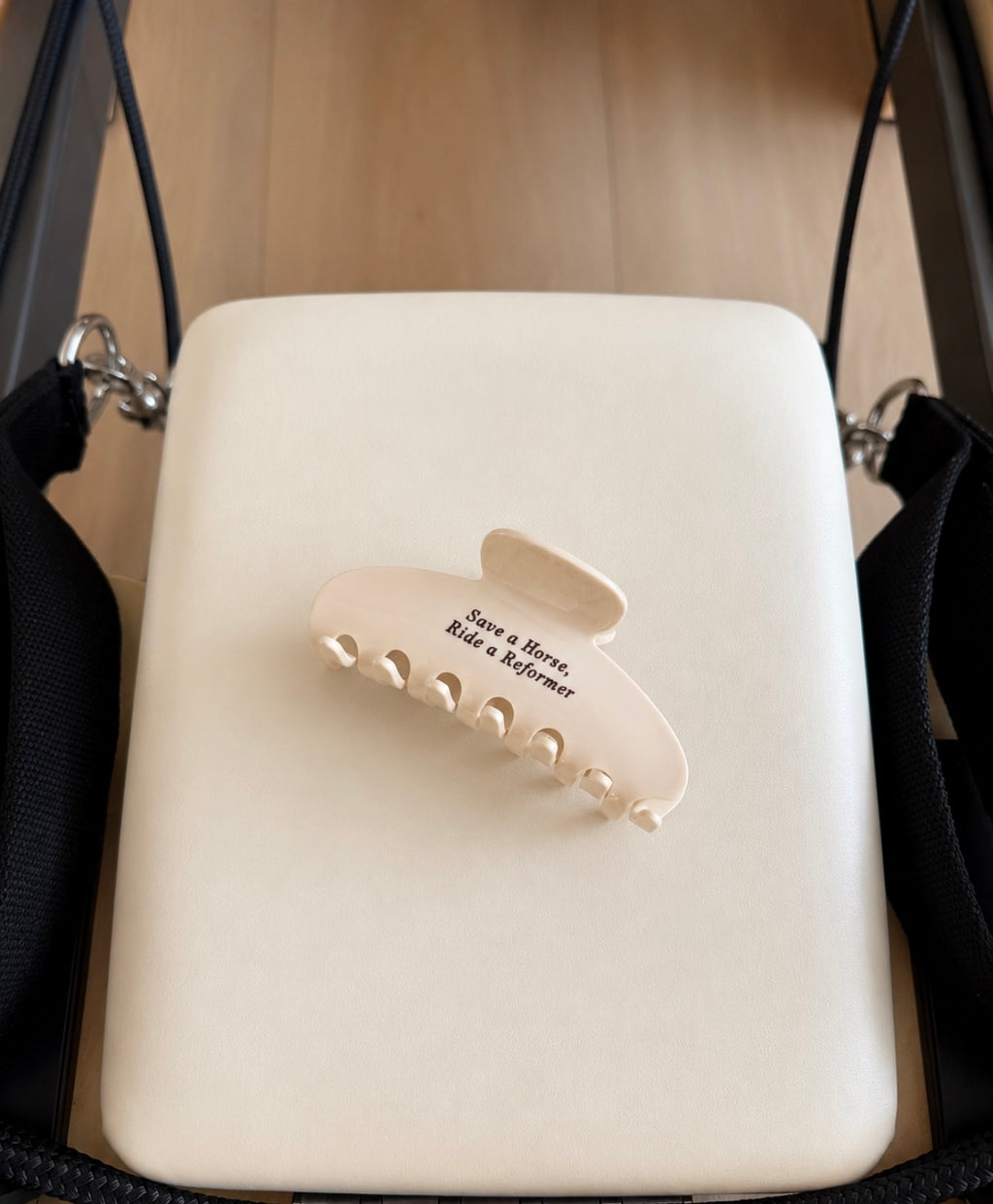 Cream claw clip with brown text saying “save a horse, ride a reformer” on a white reformer background 