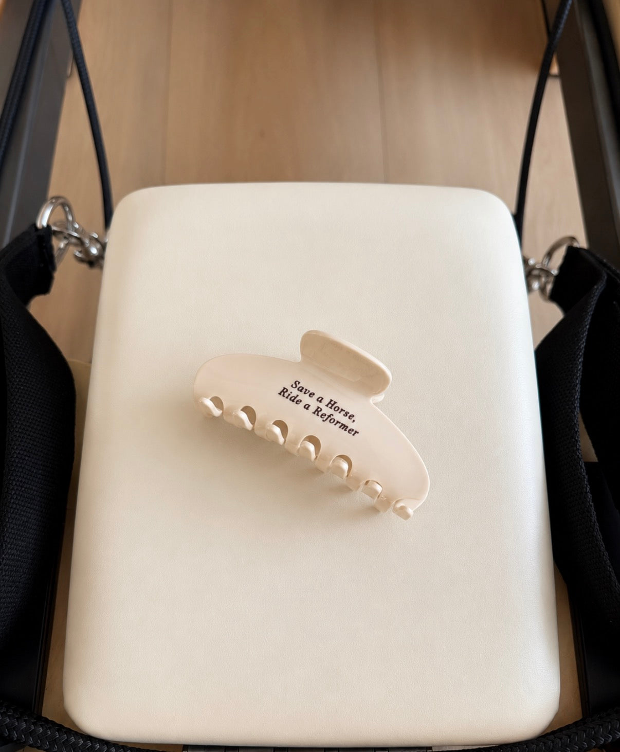 Cream claw clip with brown text saying “save a horse, ride a reformer” on a white reformer background 
