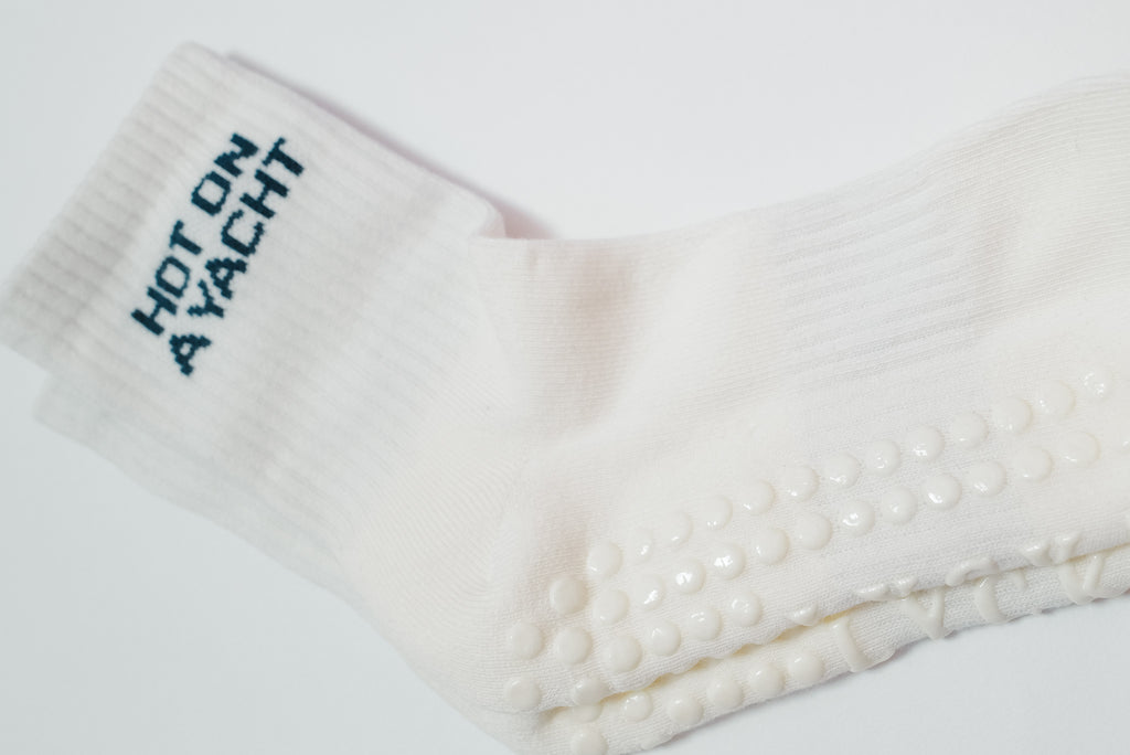 white sock in blue text "hot on a yacht" with white grips on a white background
