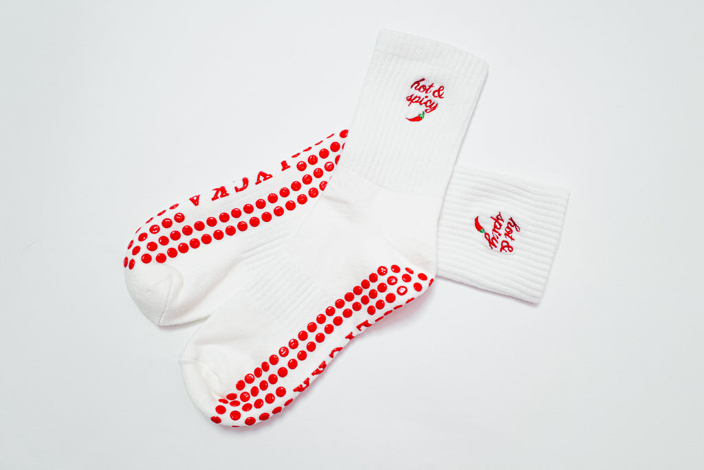 White socks with red text saying “hot and spicy” with a red chili pepper, red polka dot grip pattern and text on a white background