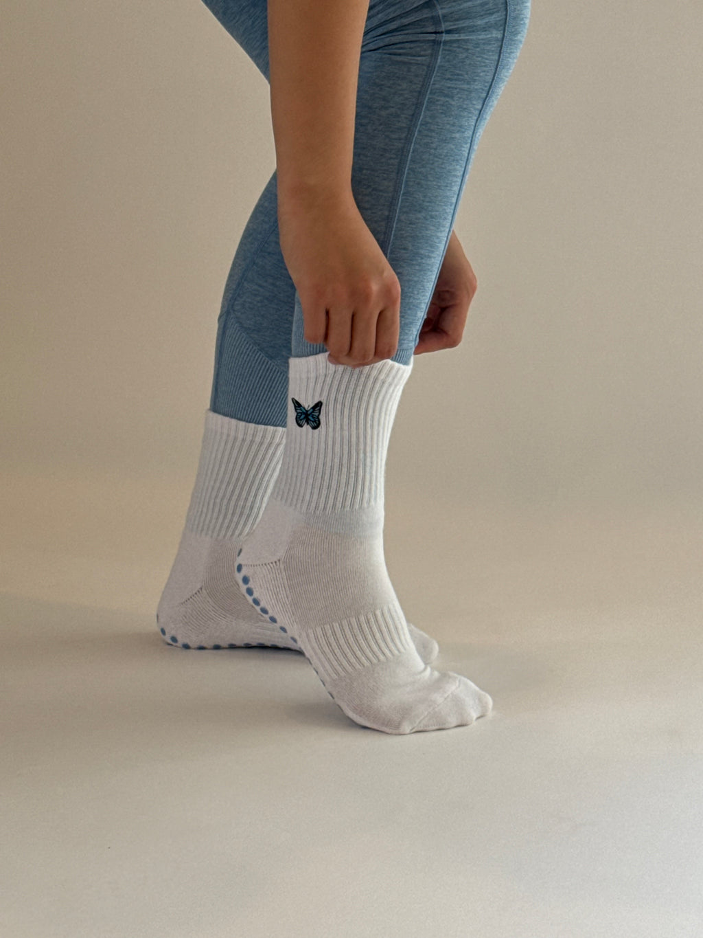 Person wearing a white crew grip sock with a blue butterfly logo on the ankle