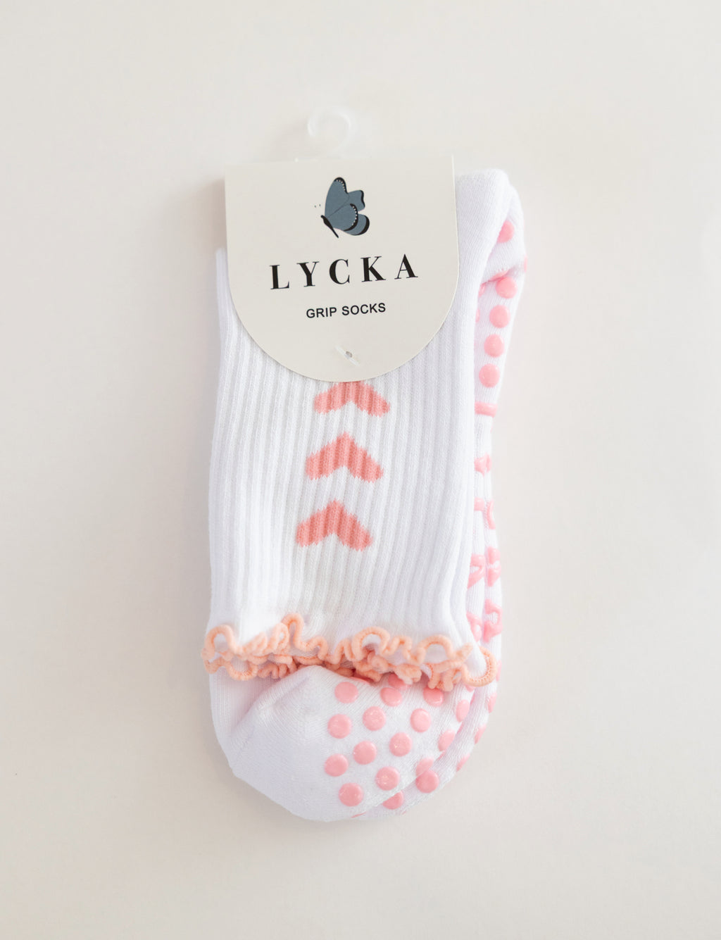 White sock with pink hearts and grip dots and text 'LYCKA' on a beige background