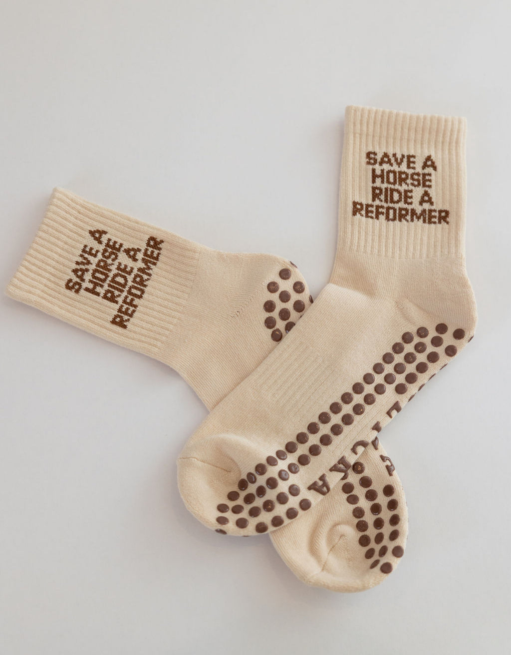 Beige socks with text saying "save a horse ride a reformer" and non-slip grips on a light gray background