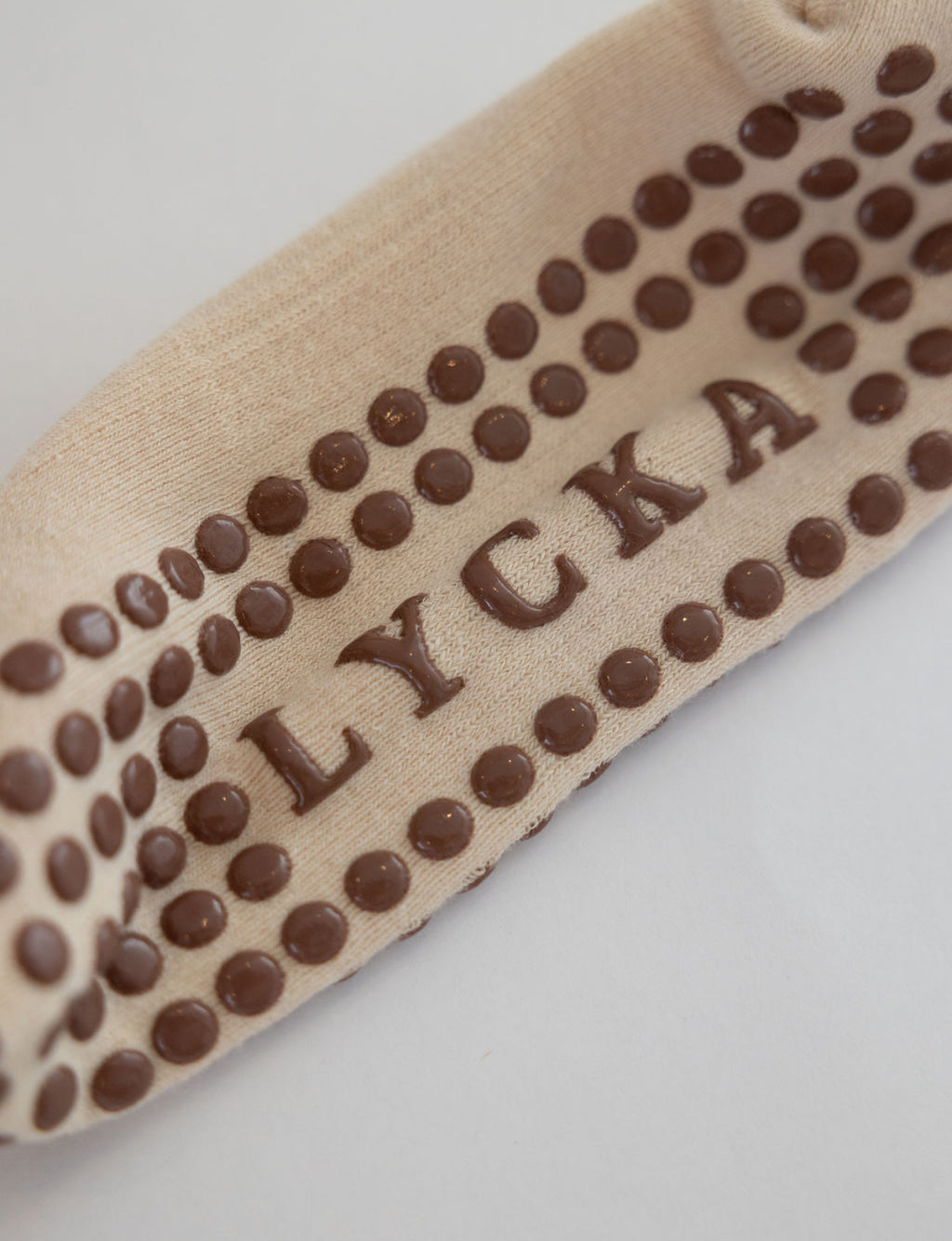 Close-up of a beige grip sock with 'LYCKA' branding on a light gray background