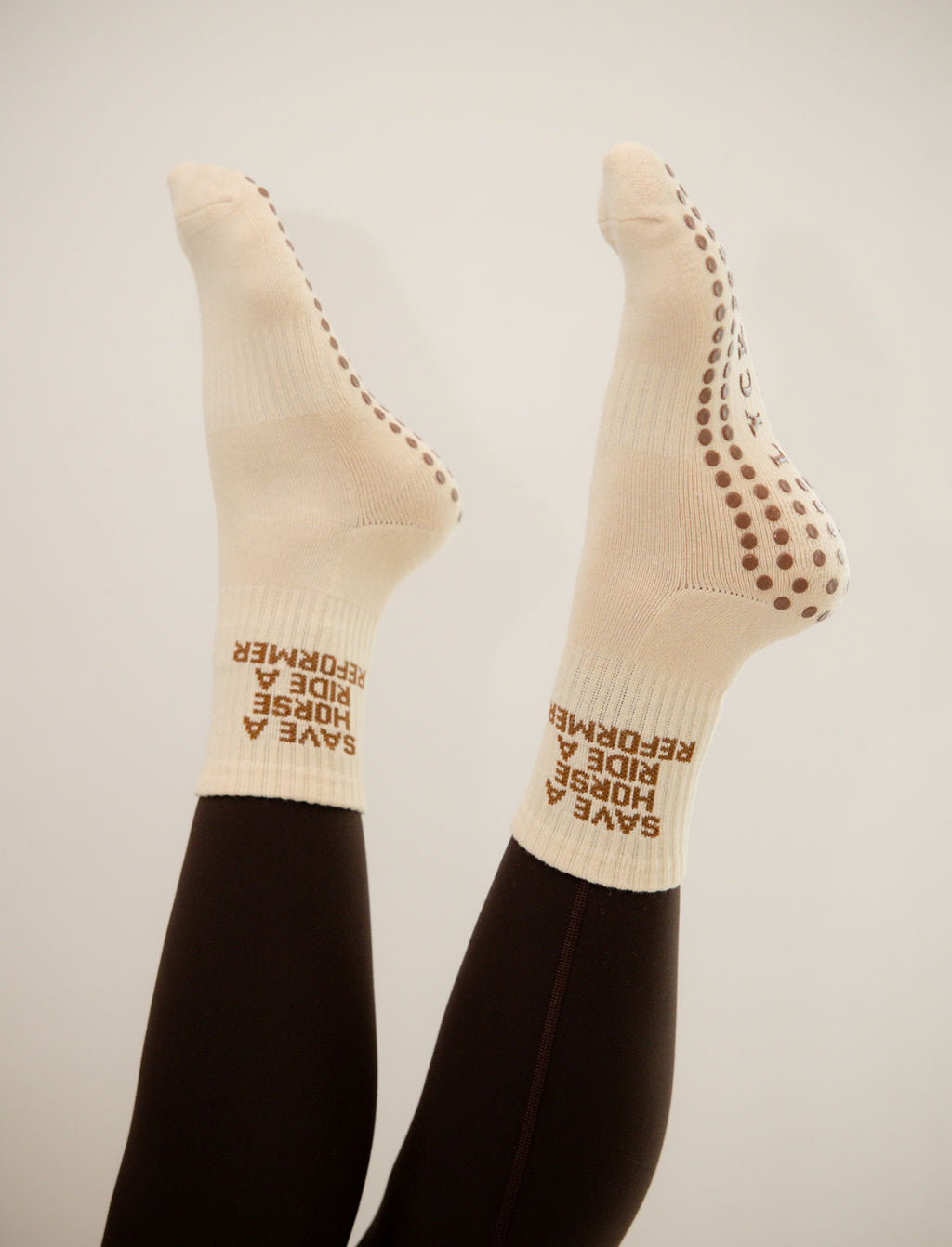 Beige socks with text "save a horse ride a reformer" worn by a person on a plain background