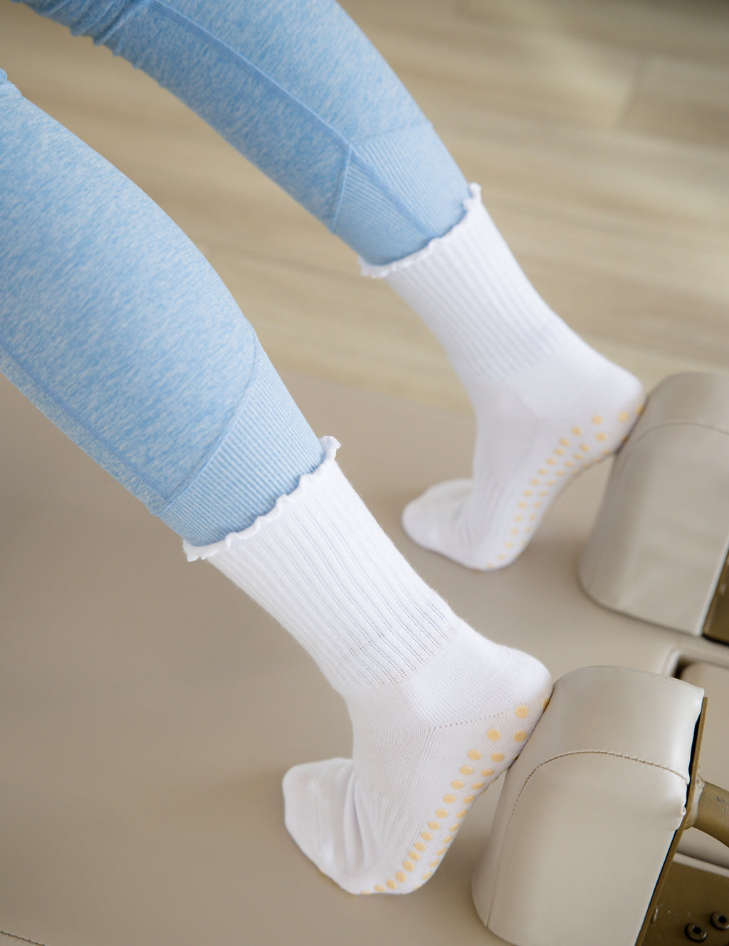 White socks with yellow grips worn by a person using a reformer machine.