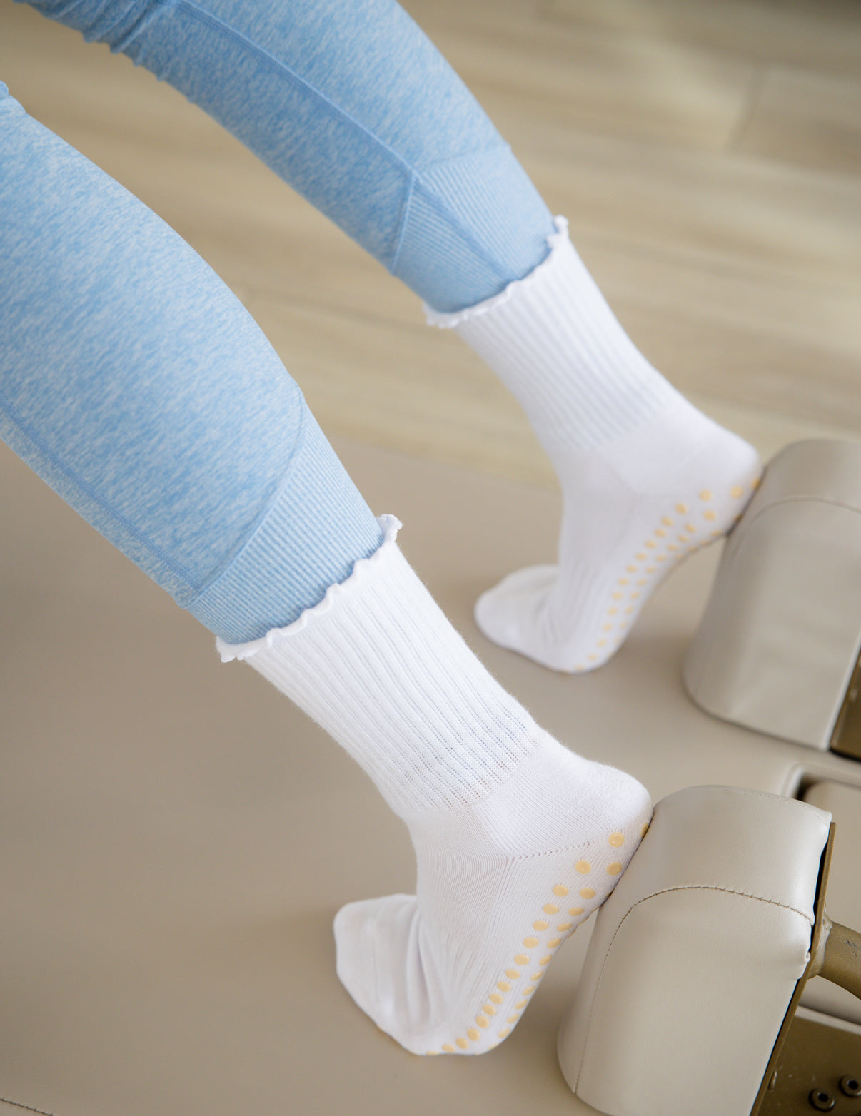 White socks with yellow grips worn by a person using a reformer machine.