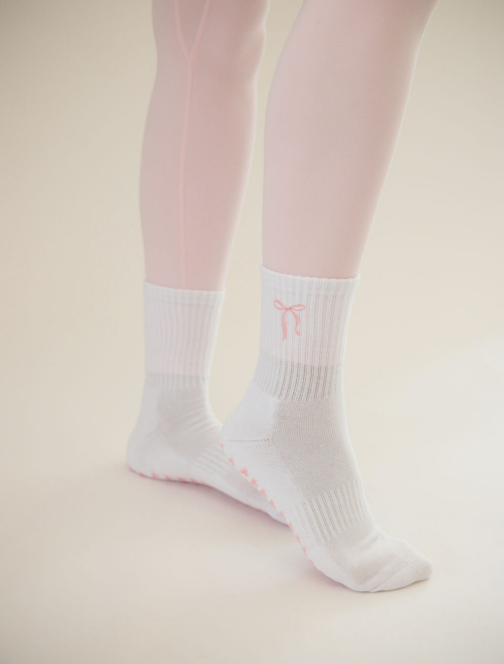 White socks with a pink bow logo worn with pink tights on a beige background