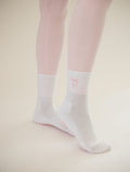 White socks with a pink bow logo worn with pink tights on a beige background
