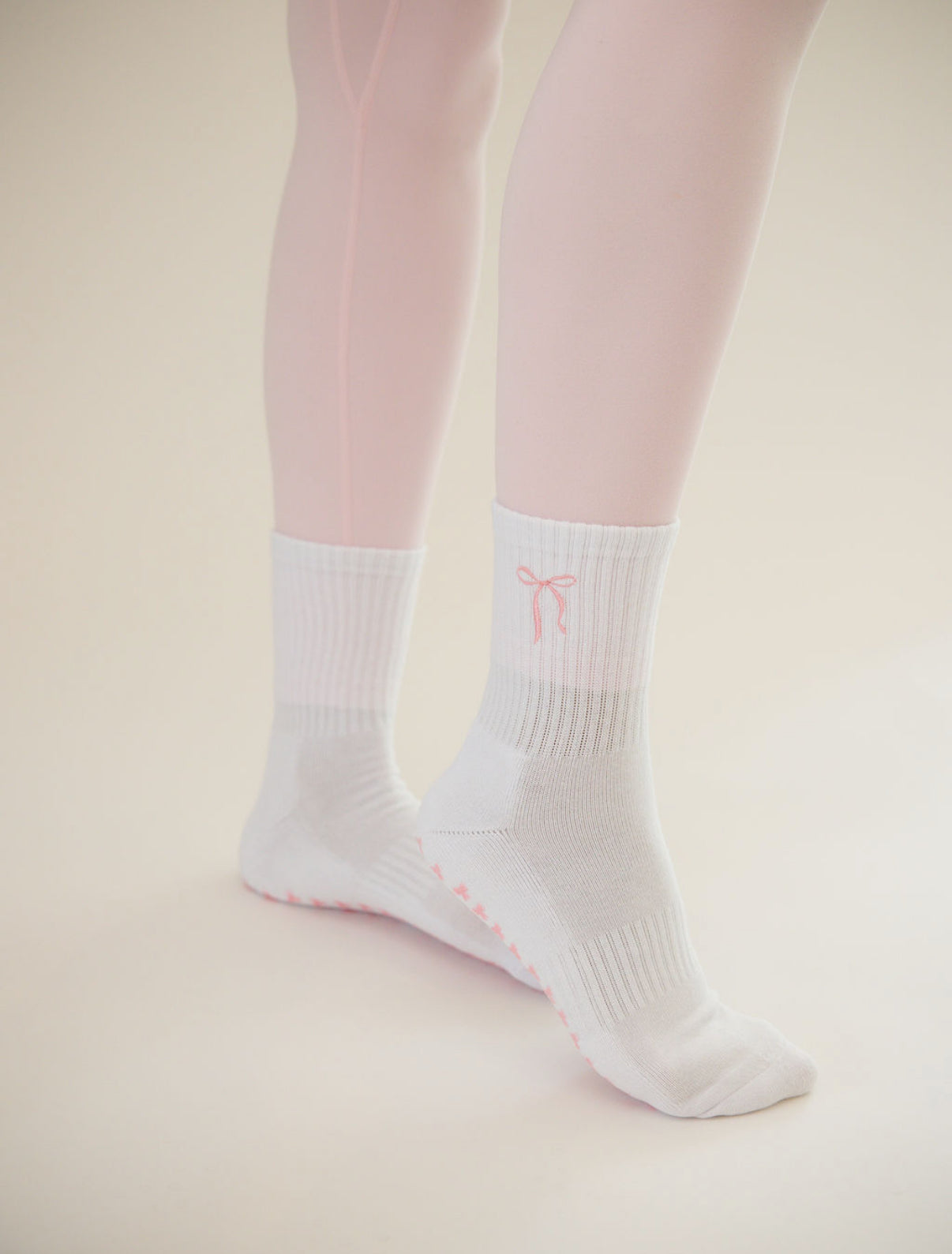 White socks with a pink bow logo worn with pink tights on a beige background