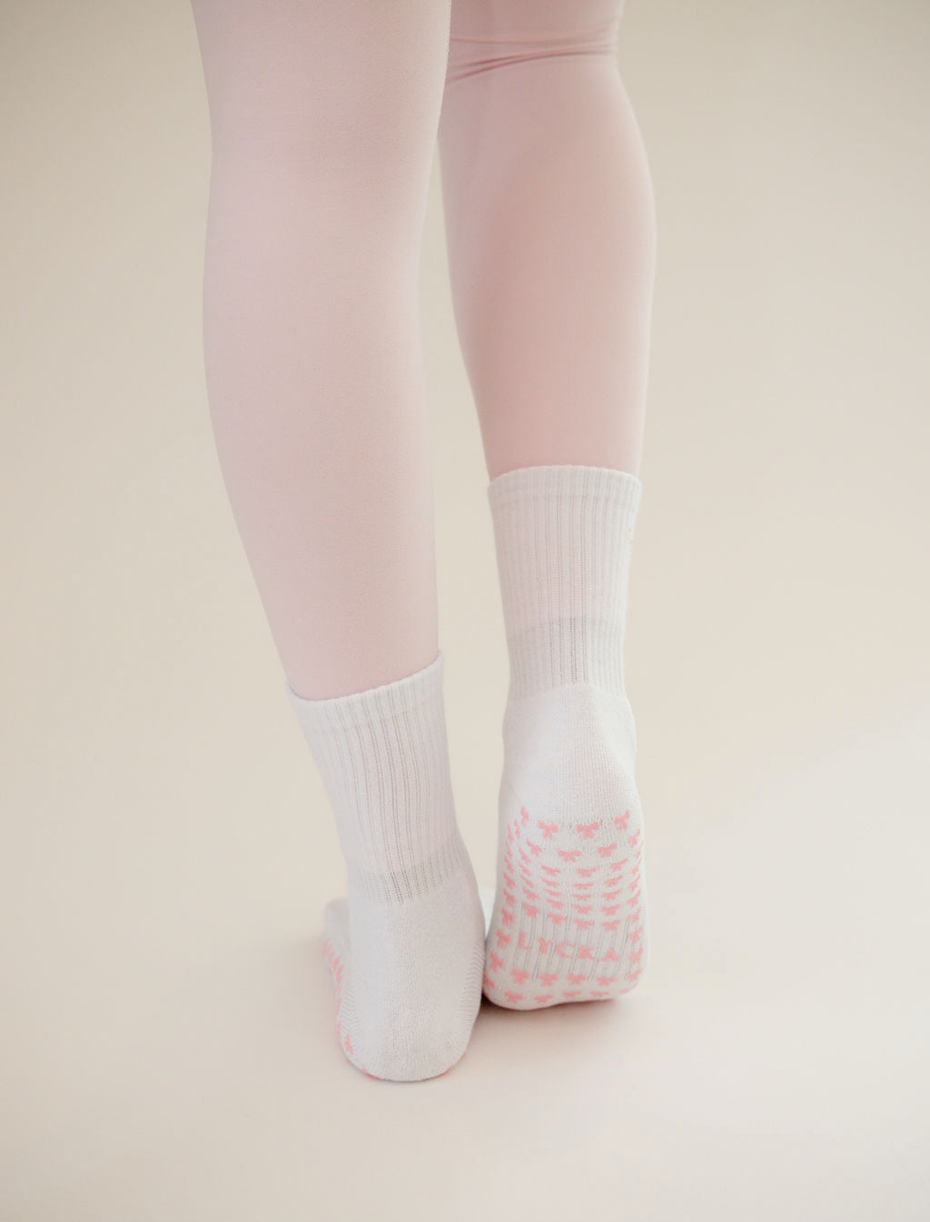 White socks with pink bow grips worn with light pink tights on a beige background