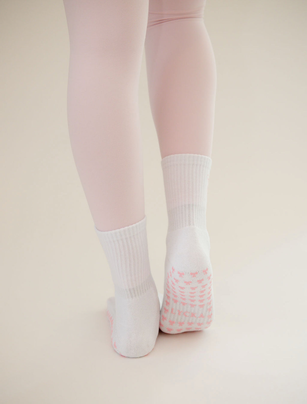 White socks with pink bow grips worn with light pink tights on a beige background