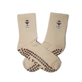 A pair of cream-colored grip socks with brown silicone dots on the sole and heel, featuring a small cocktail graphic with an 'R' on the side.