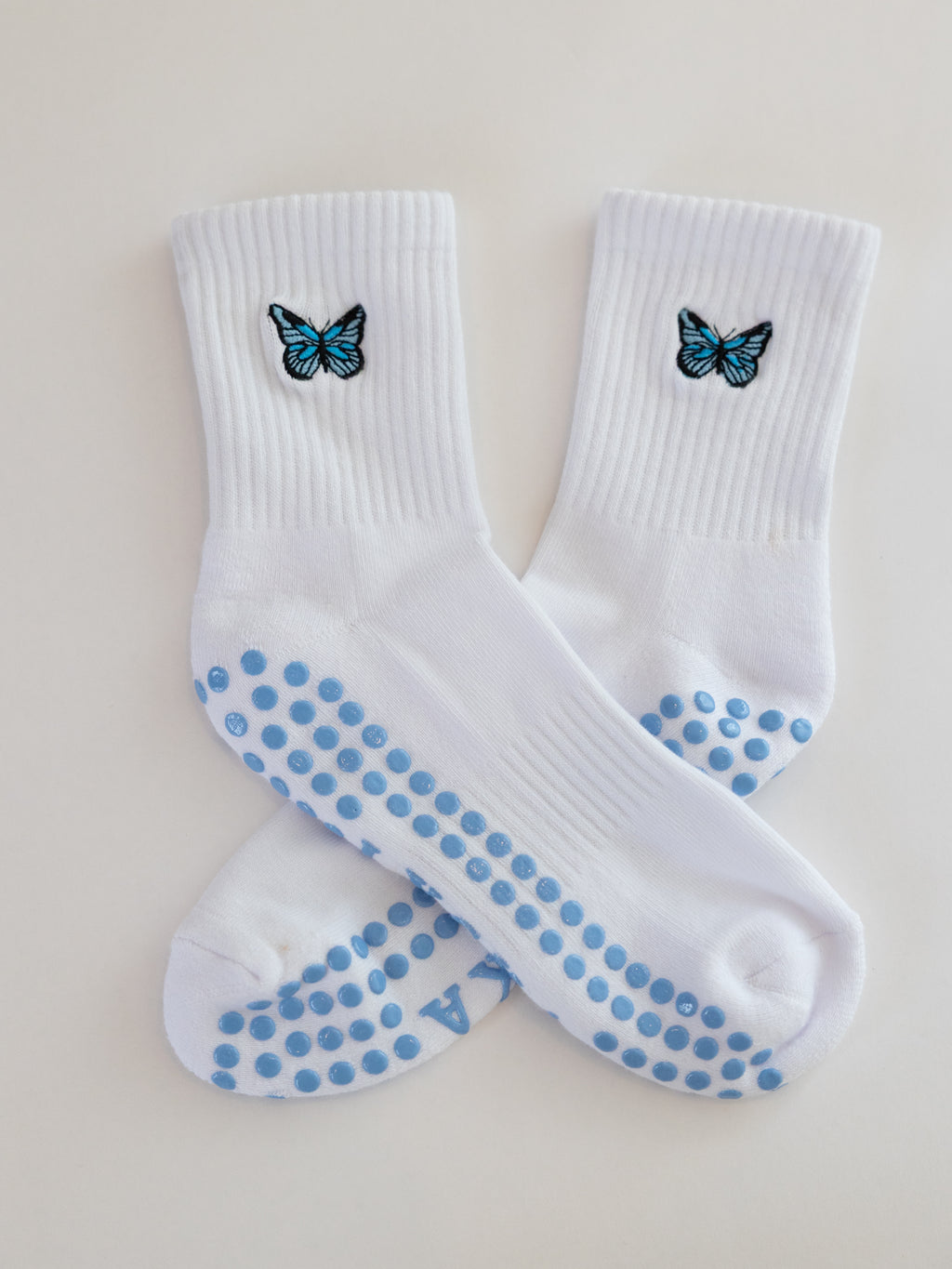 White socks with blue butterfly designs and blue grip dots on a cream background