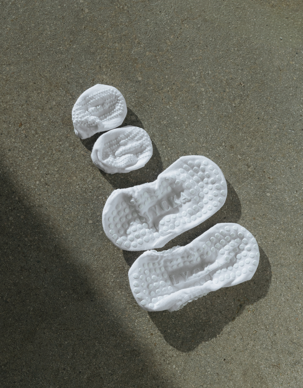 2 pairs of white grip socks arranged diagonally on a gray concrete surface.
